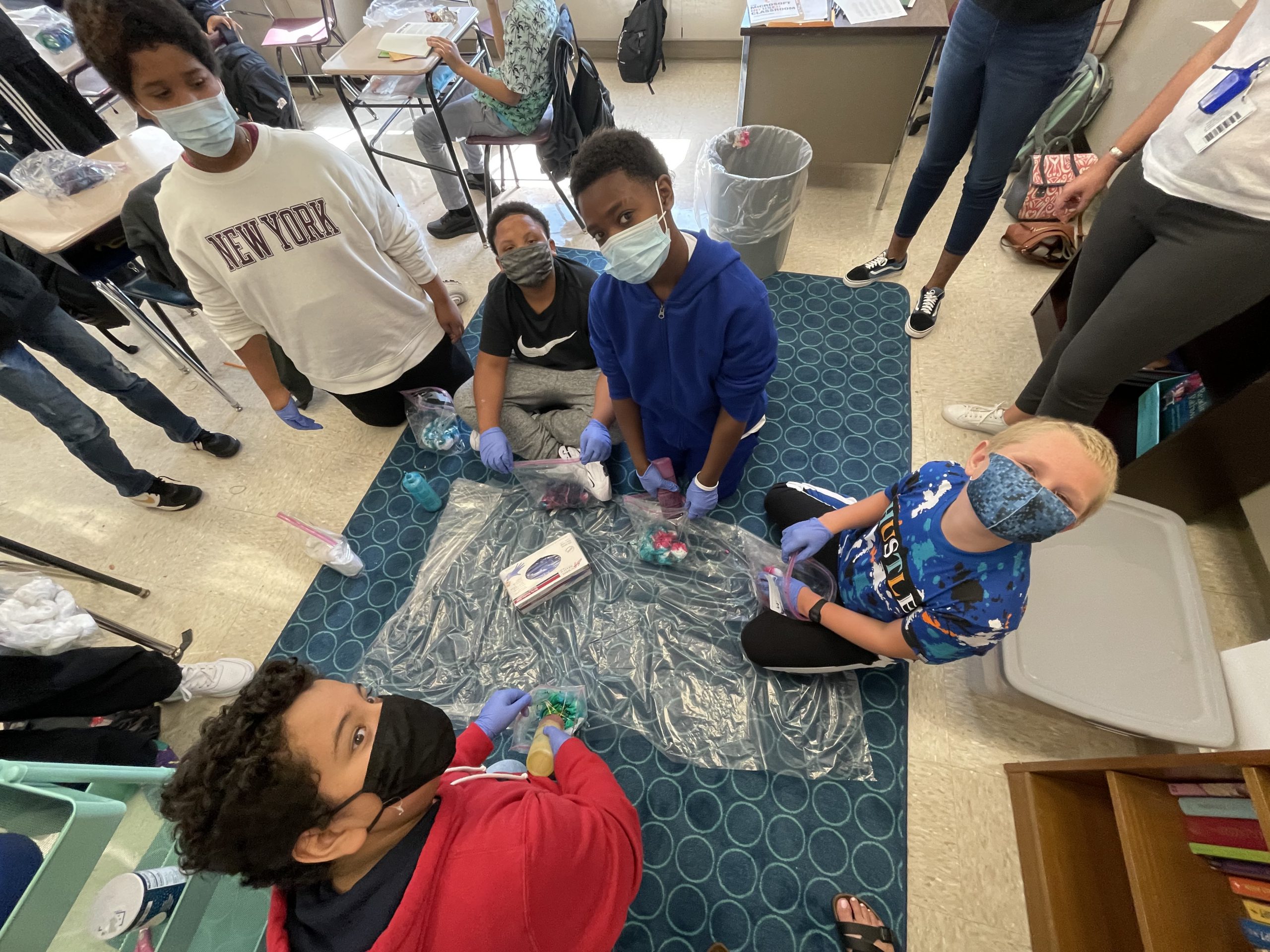 a group of students are crowded on the floor working on tie dying t-shirts