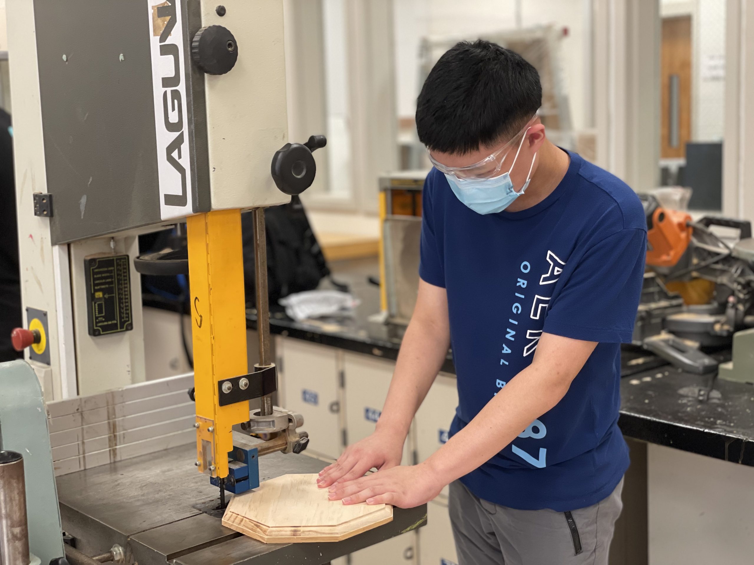 a male student is standing in front of an industrial saw, looking down and working on a project