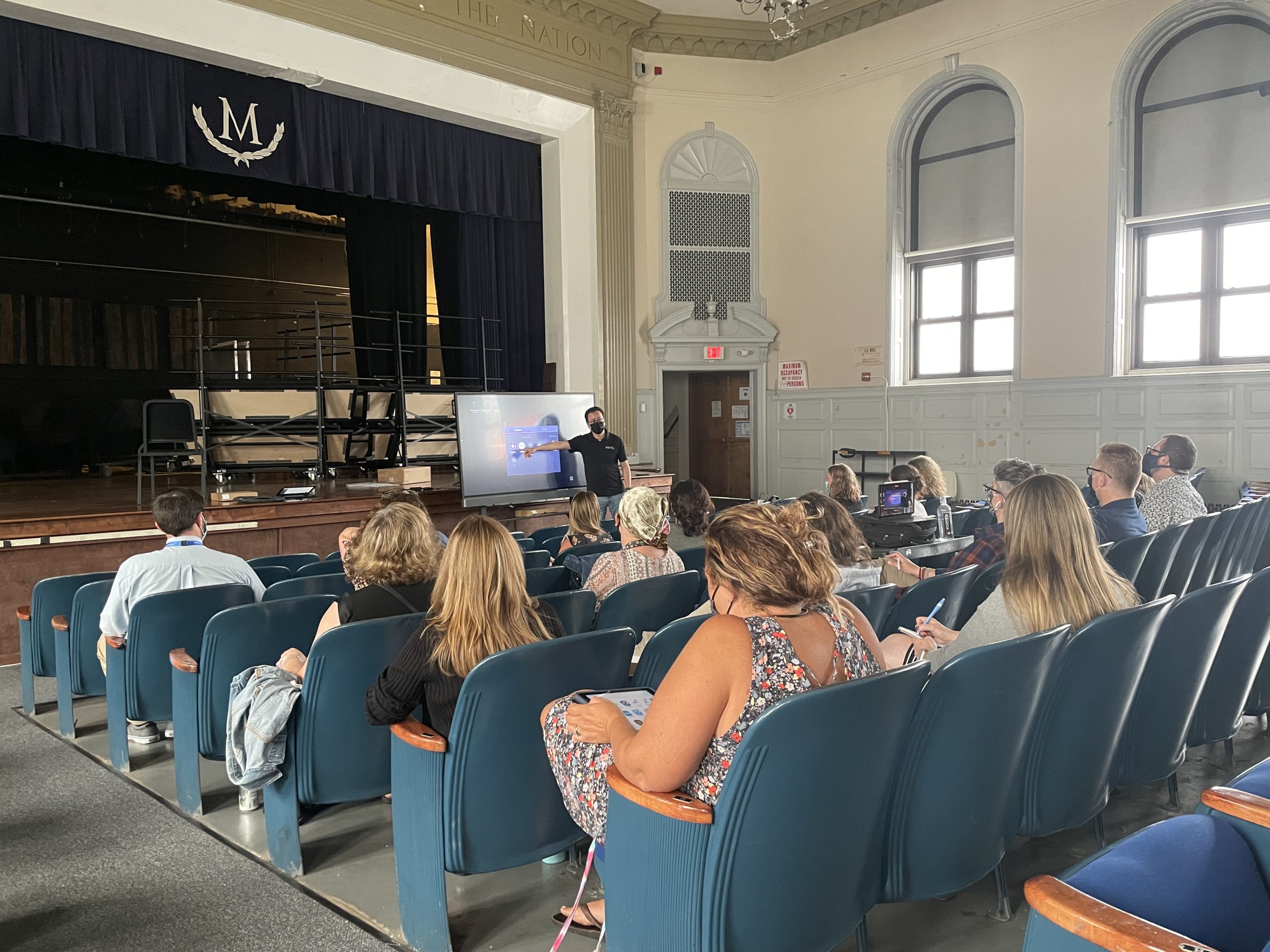 a room full of teachers are seated and watching a man present 