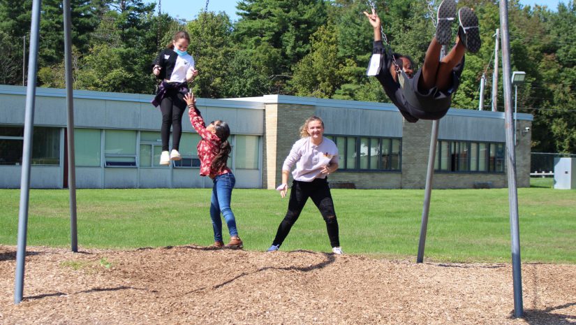 two girls are on swings, and two girls are pushing them