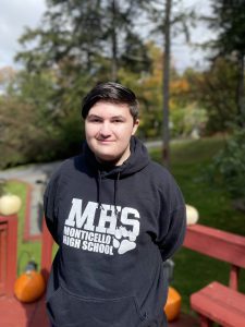 William is standing outdoors wearing a black sweatshirt and smiling 