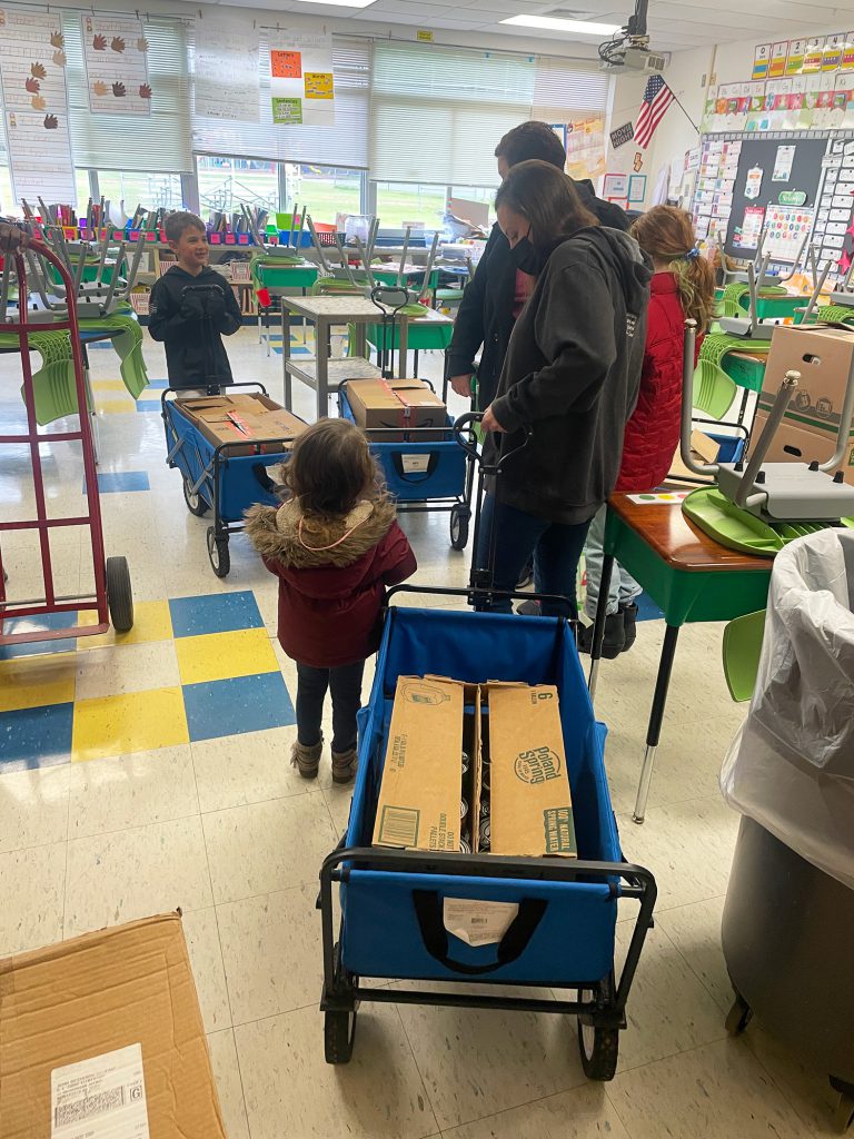 Adult and child wheeling a wagon with food donations into the classroom.