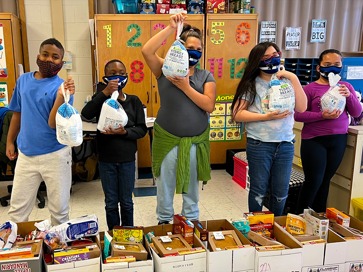 Students and teacher holding turkey donations for the Thanksgiving Food Drive in a classroom.