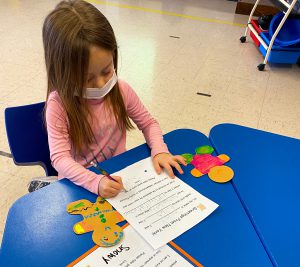 Girl in kindergarten writing a letter describing her gingerbread person.