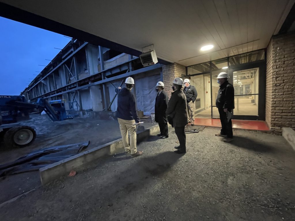 a group of admins and architect reps are standing in a courtyard with steel beams in the background 