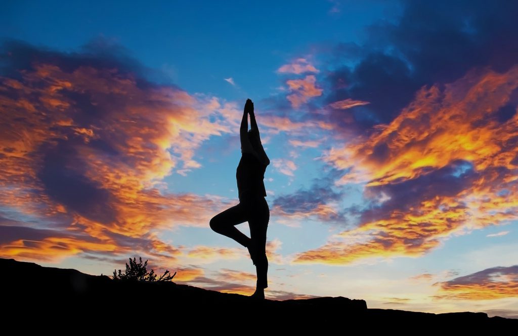 silhouette of person doing a standing yoga post with the sunset in the background