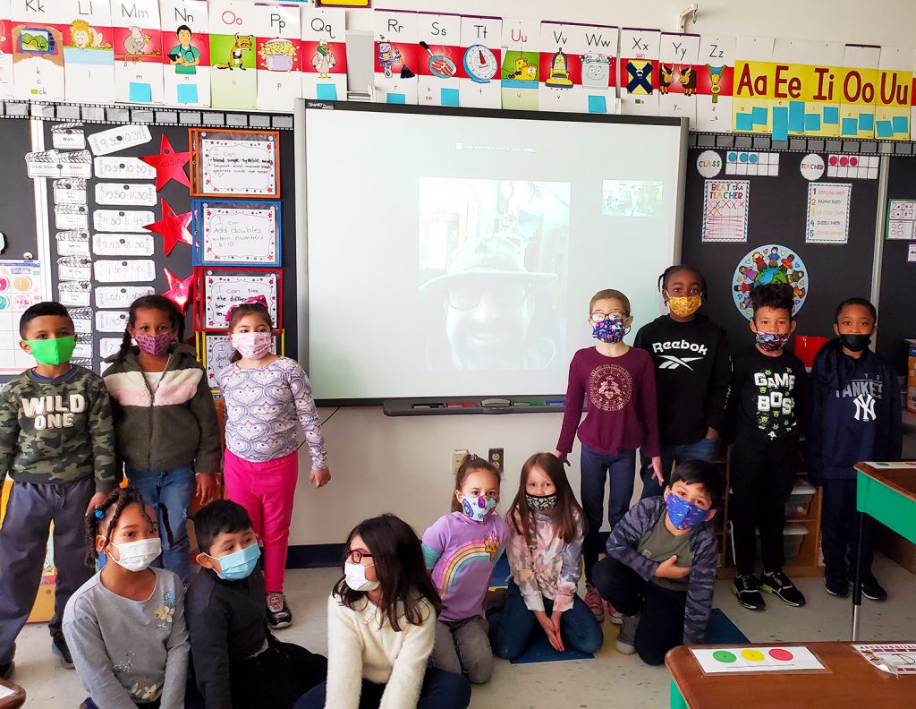 Ms. Dutcher and Miss D’Agata’s first grade class with Retired US Army Sergeant Michael Epstein. Epstein can be seen on video/Zoom on the Smartboard behind the students. 