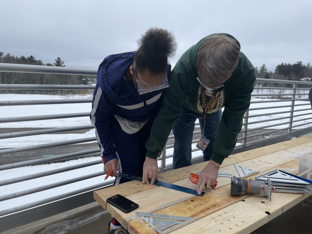 a teacher is helping a student measure a piece of wood 