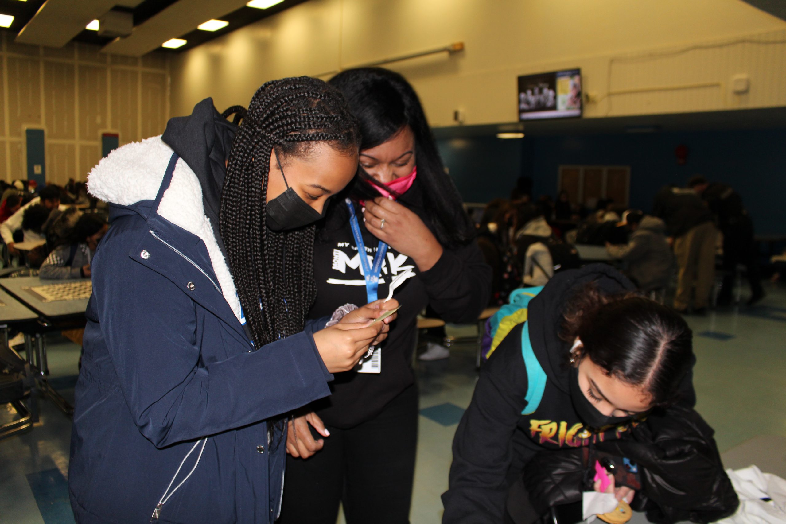 a girl is signing a sheet of paper as a teacher and other student look on 