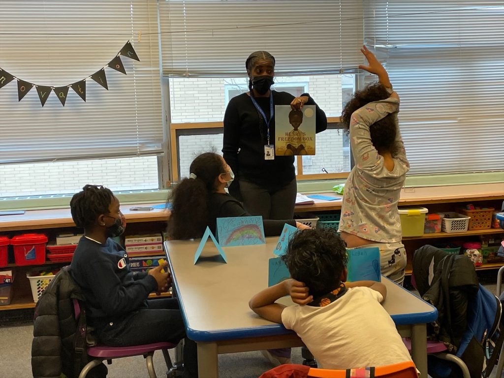 a teacher is standing in front of a classroom with a book