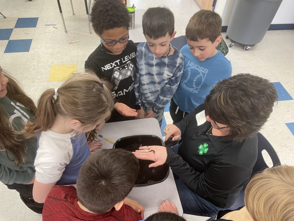 a group of students are huddling around a woman who is holding a worm in her hand 