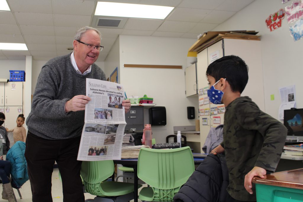 Fred Stabbert is showing the front page of a newspaper to a student who is seated 