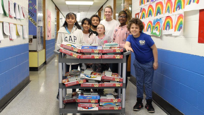 a group of students is standing with their teacher next to a cart. On the cart, there are goody bags