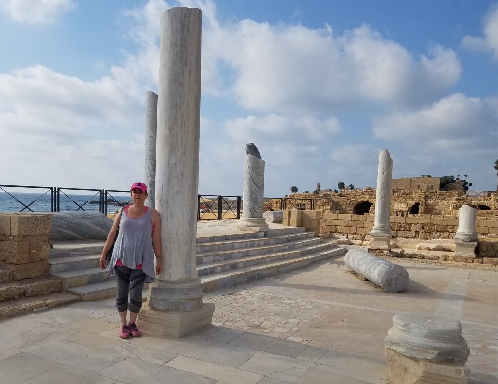 Ms. Reef is standing on a beach with old columns in the foreground. She is smiling for the camera