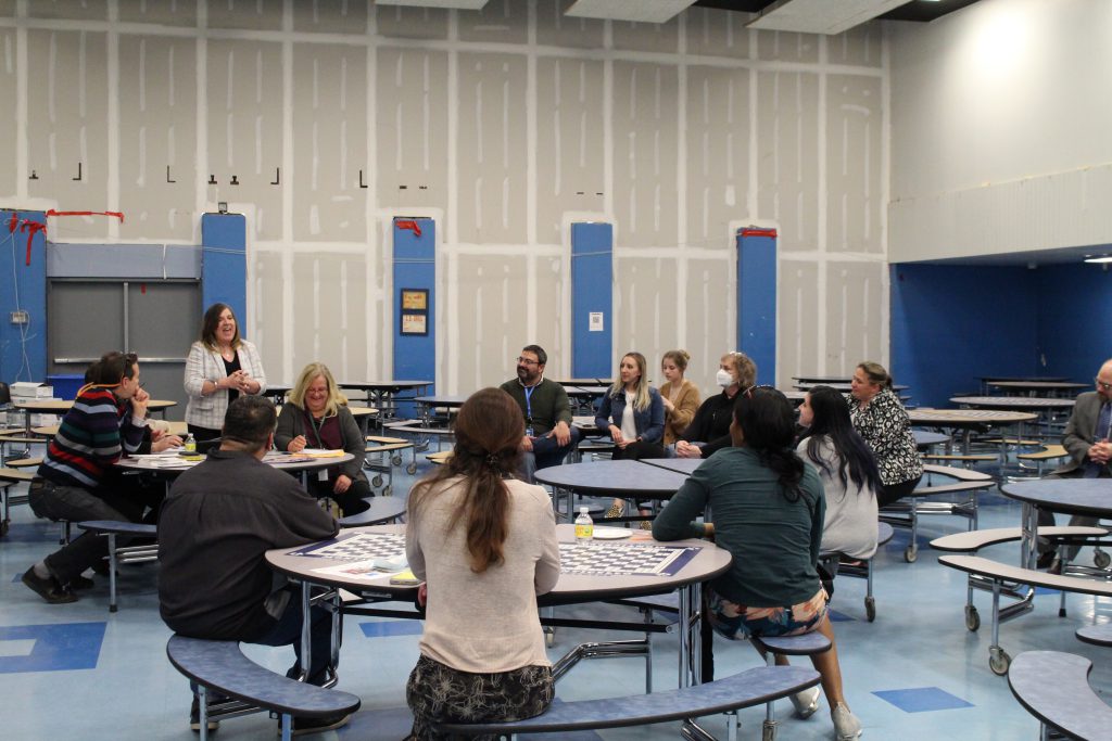 a group of adults are sitting at tables listening to a woman speak 