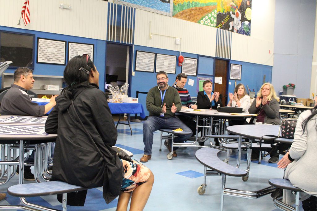 A woman is speaking to a group of people seated at tables.