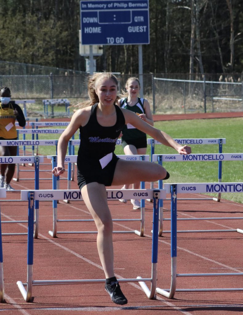 a female track athlete is jumping over a hurdle 