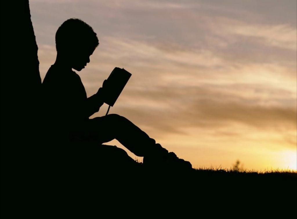 silhouette of child reading under a sunset