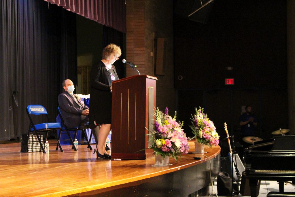 Lori Orestano James is speaking at the podium on-stage at the Hall of Distinction ceremony.