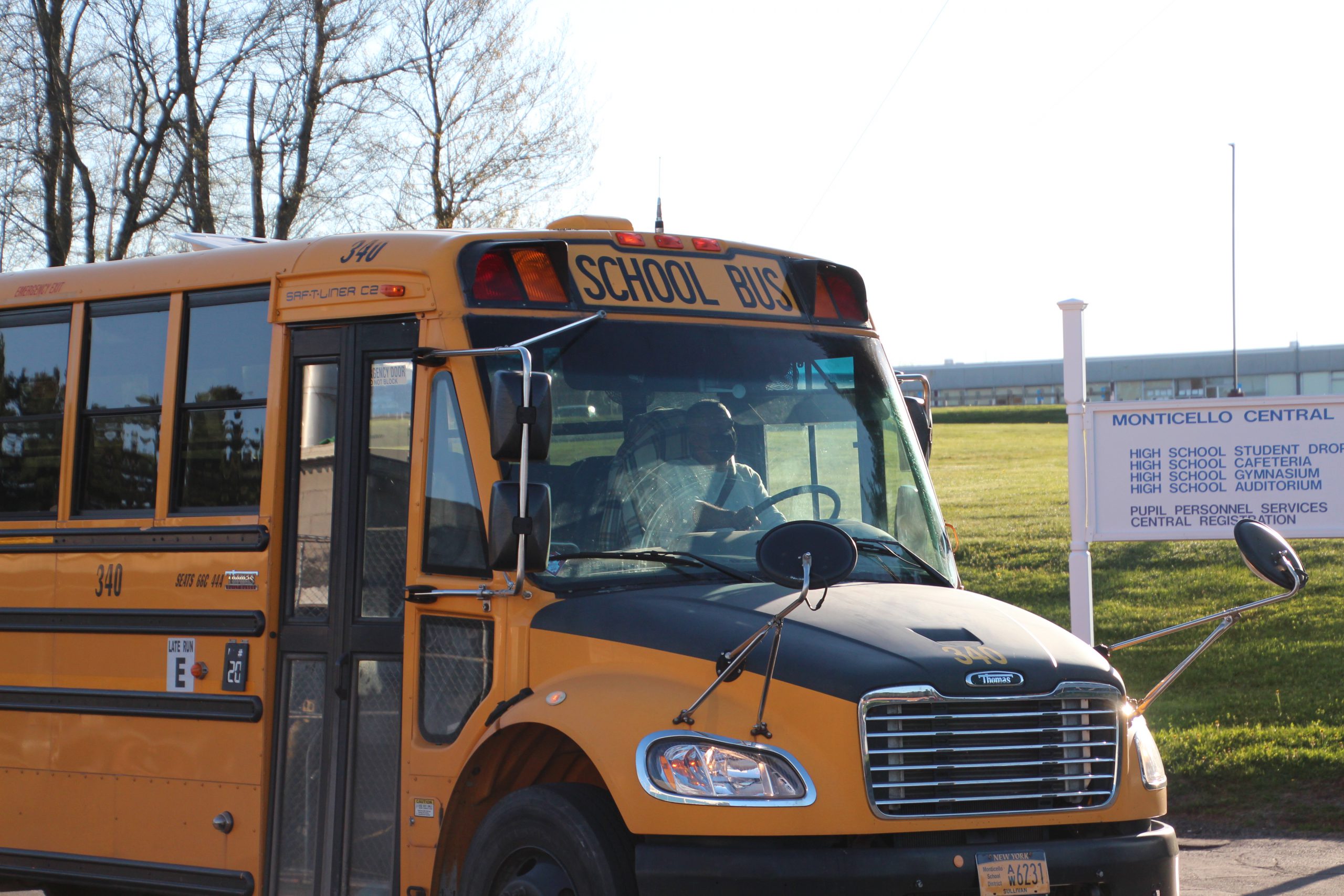 A person is driving the bus in the parking lot of the school.