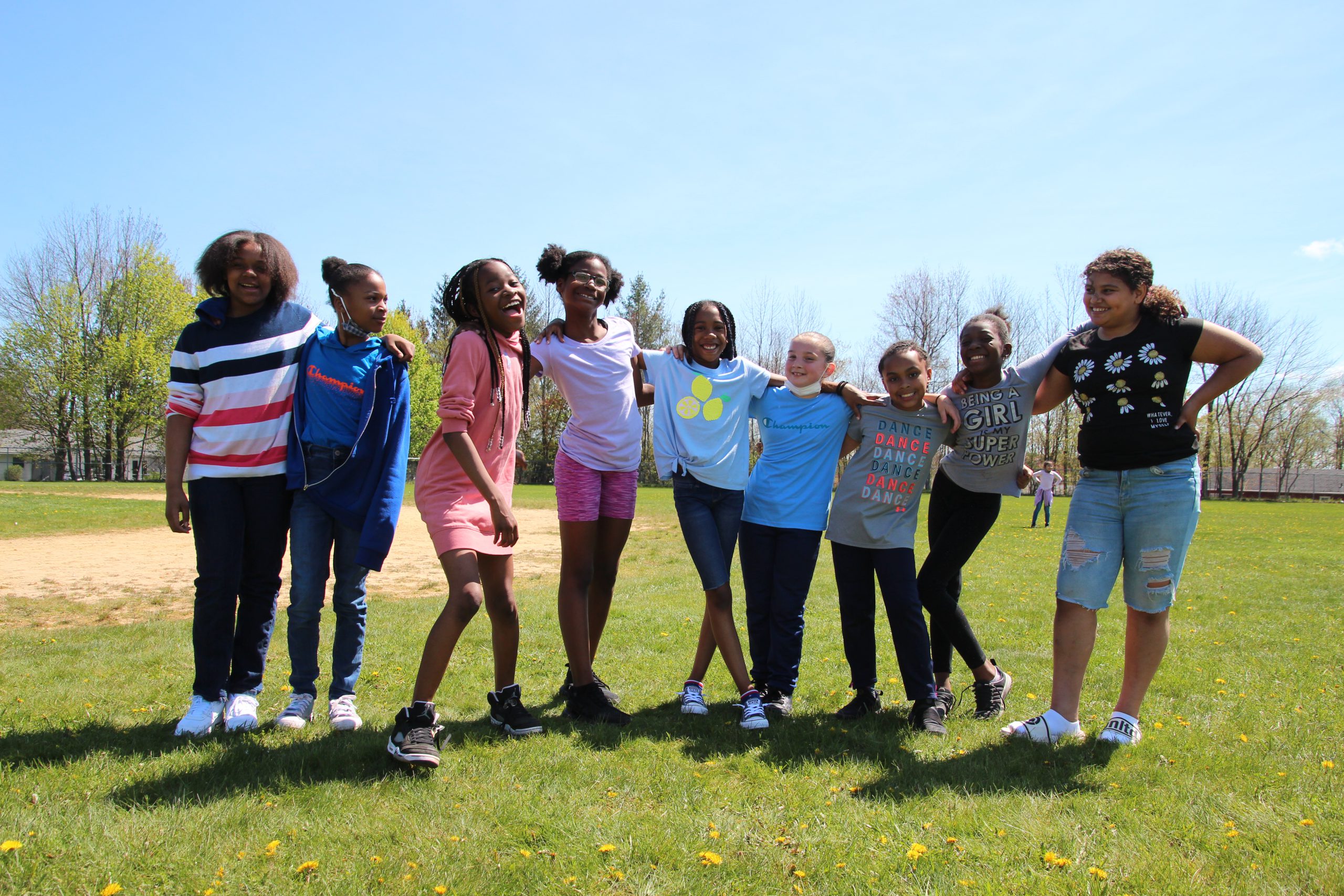 A group of 9 elementary students standing together outside and smiling for a group picture.