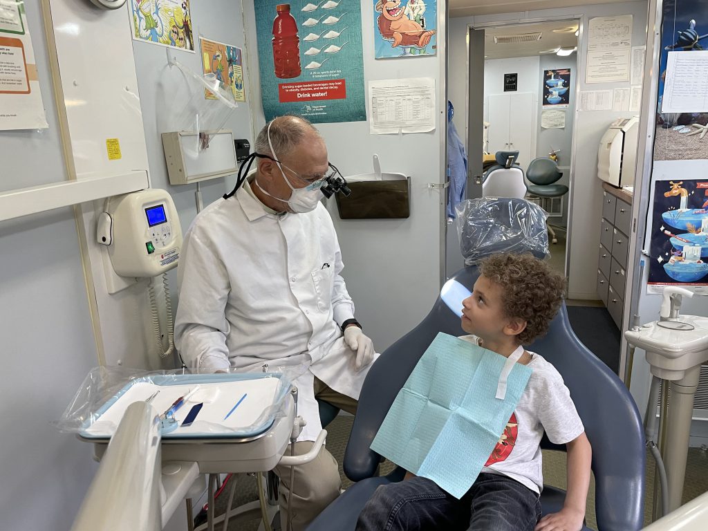 a young boy is sitting in a dental chair and smiling at a dentist, who is seated beside him