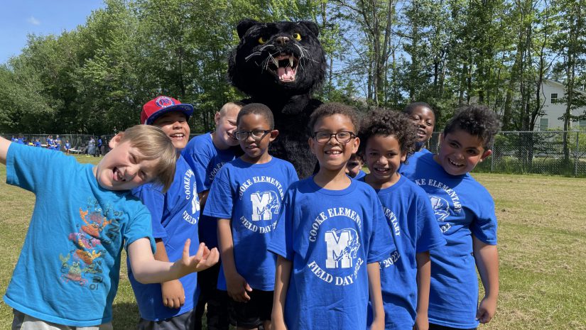 a group of young male students wearing blue Cooke ELementary shirts are posing with a Panther mascot
