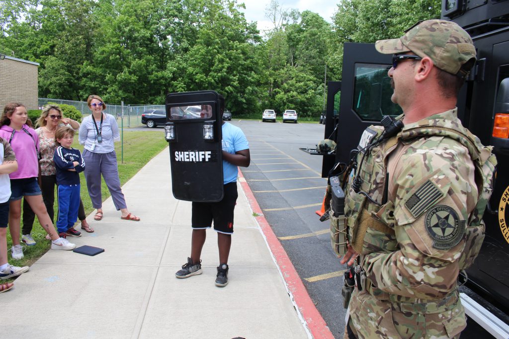 a group of students is watching deputy barrett help a student demonstrate a shield 