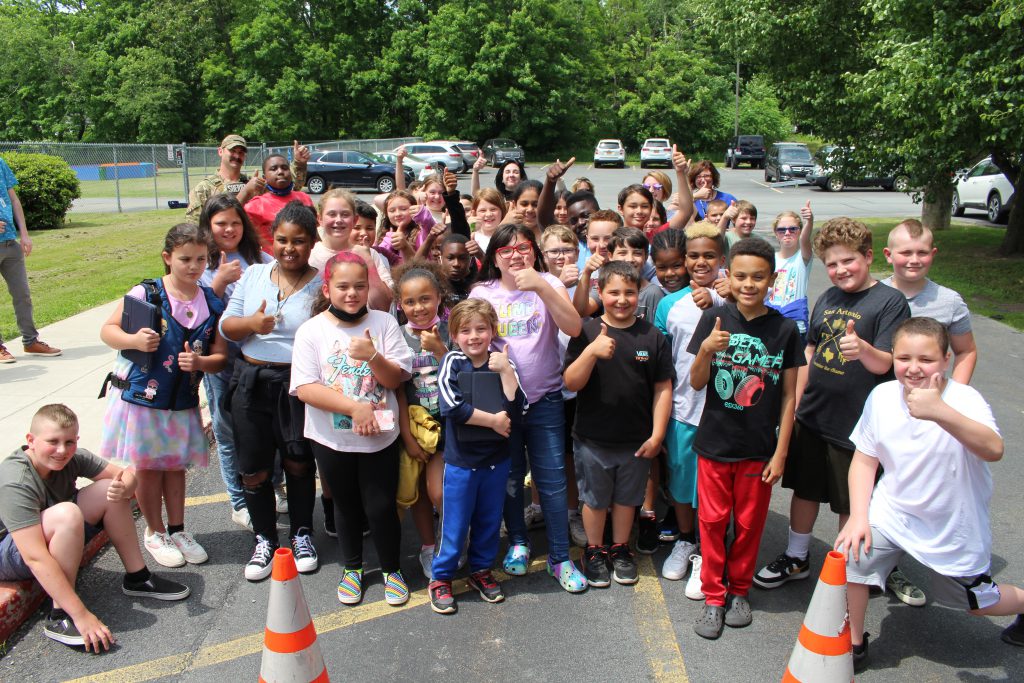 a group of students are posing outside of the armored vehicle and smiling