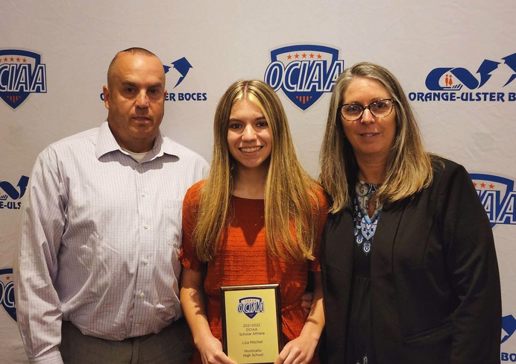 Liza Mitchell is standing with her parents holding her OCIAA award. Everyone is smiling for a picture. 