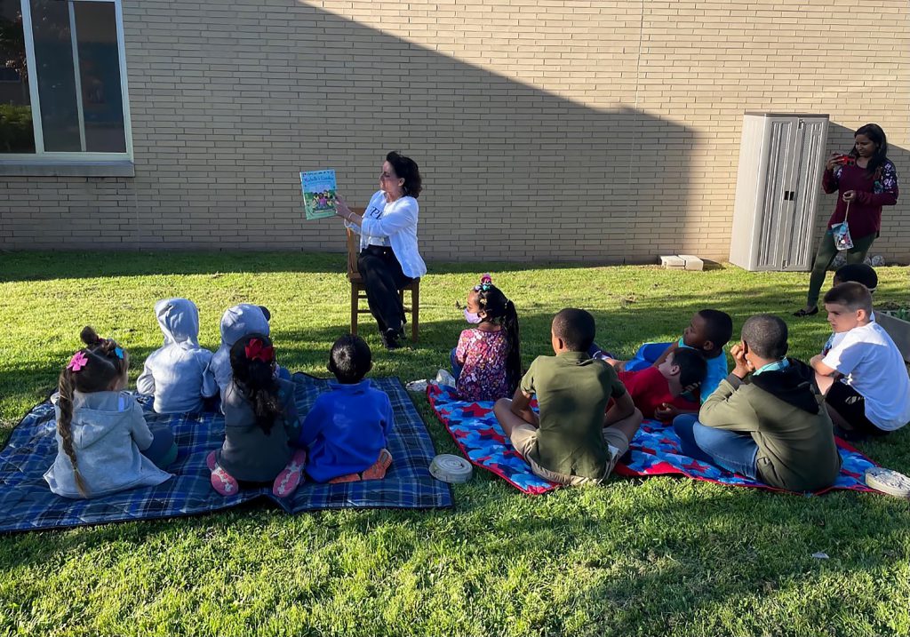 Jane Sorensen, EPIC Family Engagement Program Manager, is reading to students in the garden.