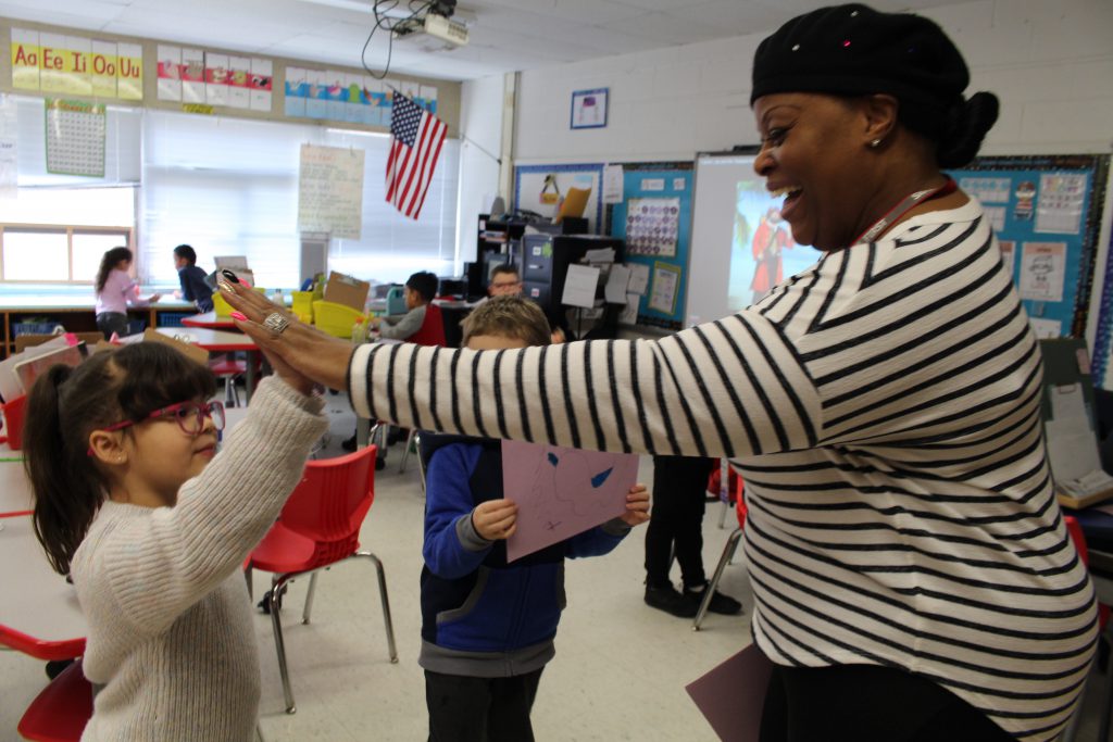 A teacher's aide is high-fiving a student in the classroom.