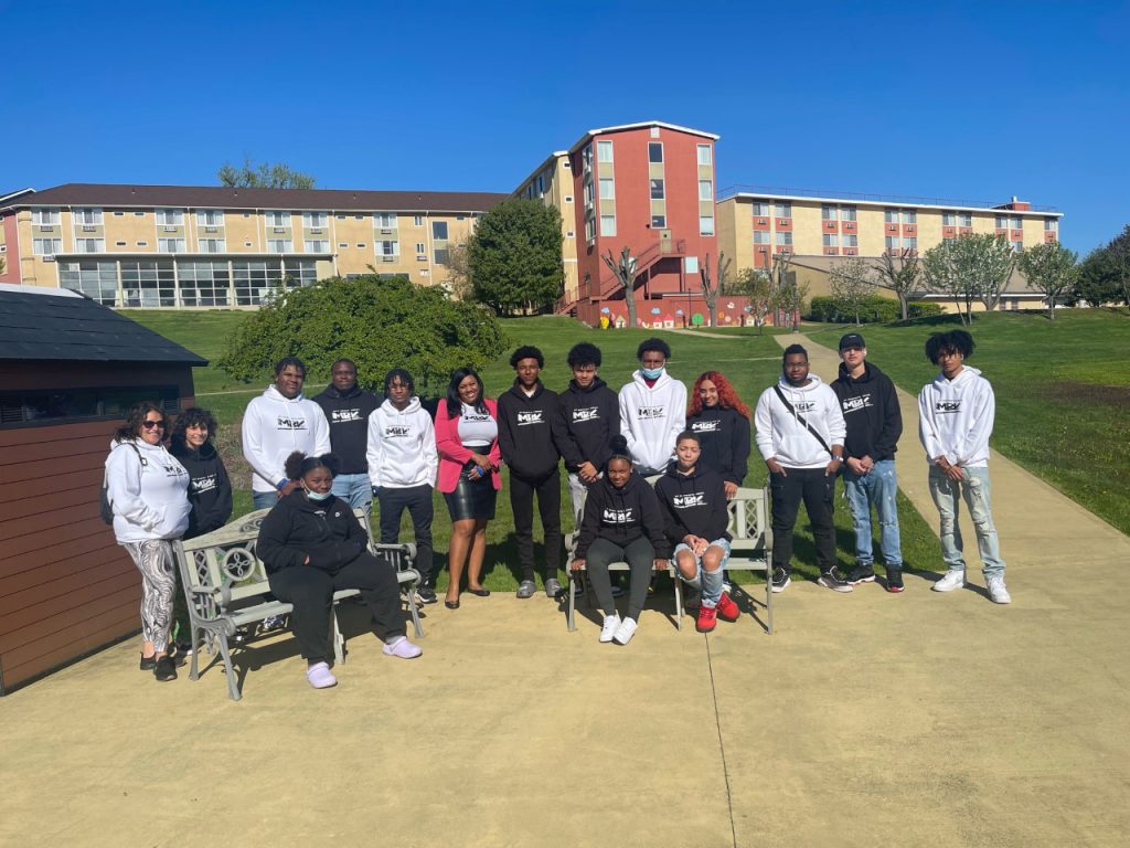 a group of students are standing in front of a hotel. They are all wearing MBK sweatshirts