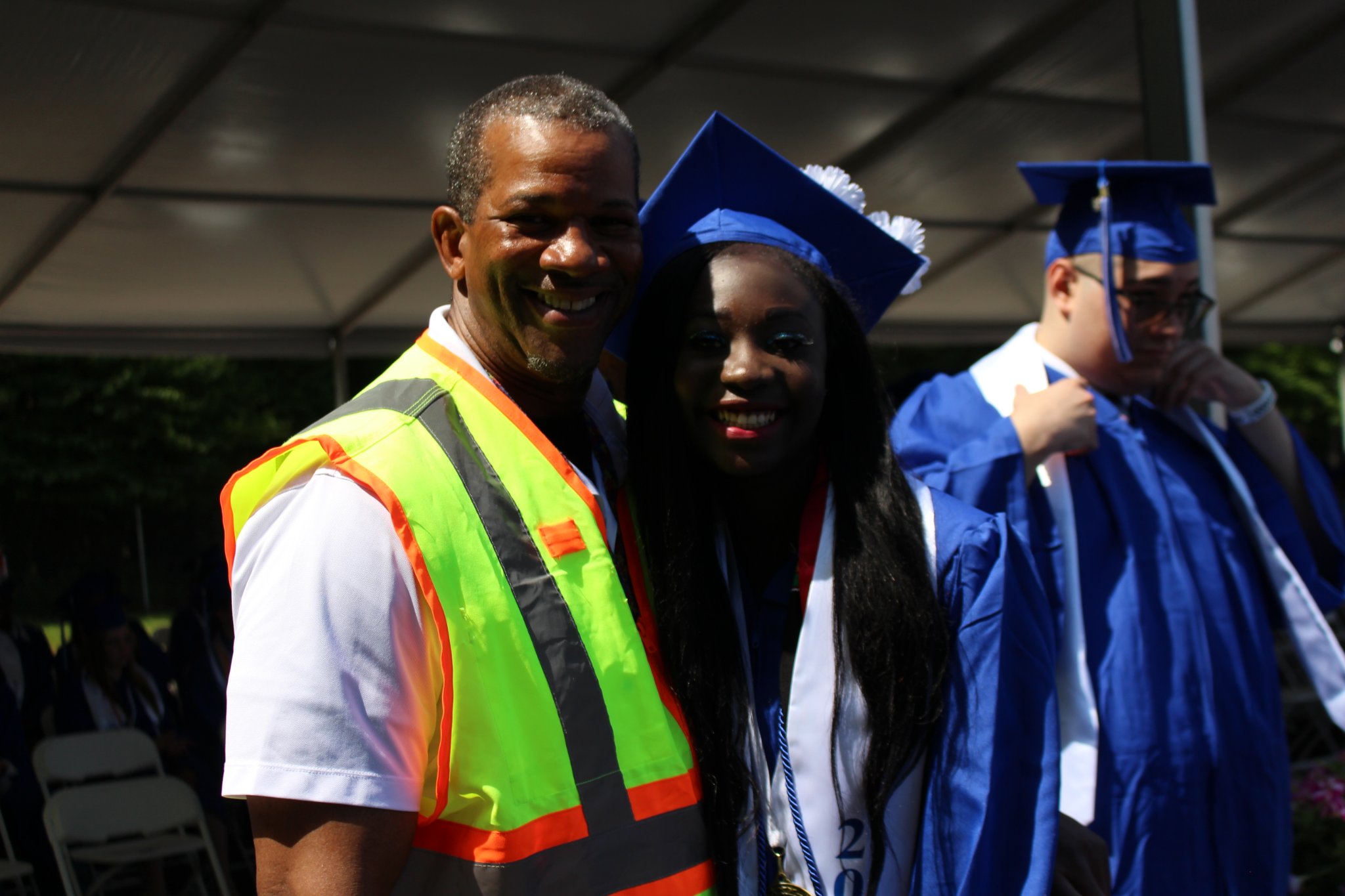 Two Monticello female security attendants are smiling for a picture together. The woman on the right is wearing a bright neon yellow reflective vest and the woman on the left is wearing a blue polo shirt with a walkie-talkie attached to it.