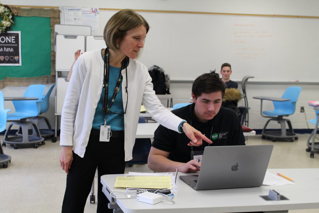 a teacher is pointing to a laptop that a student is reading on