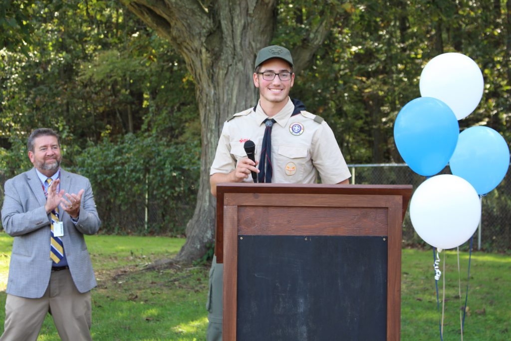 a young man in a boy scout uniform is standing at a podium holding a microphone 