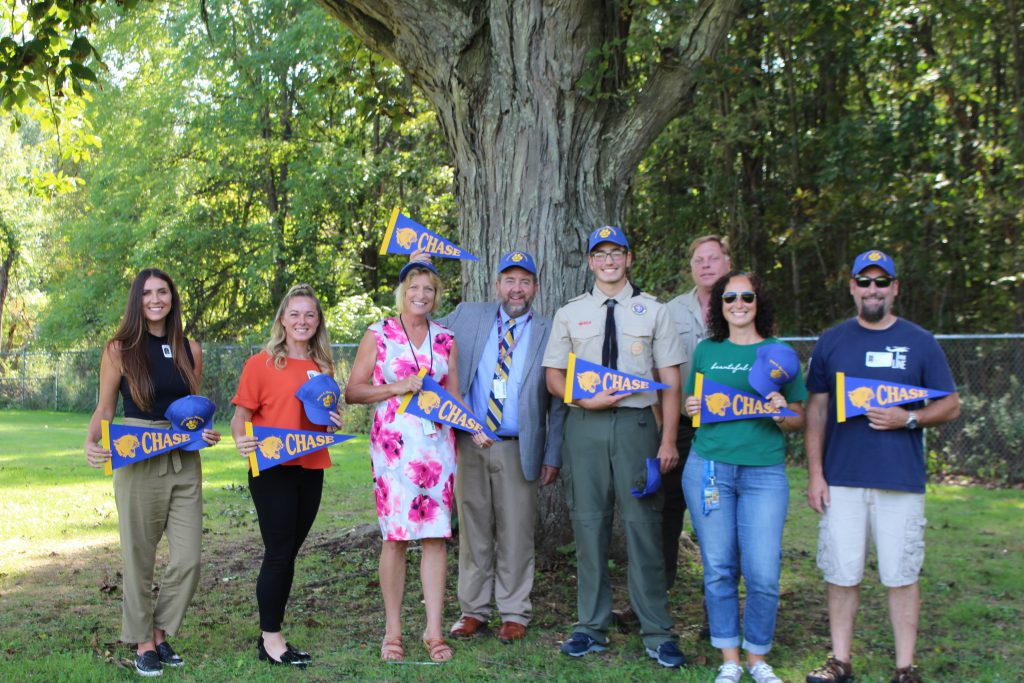 a group of people standing by a tree. They are holding up banners that say Chase Elementary 