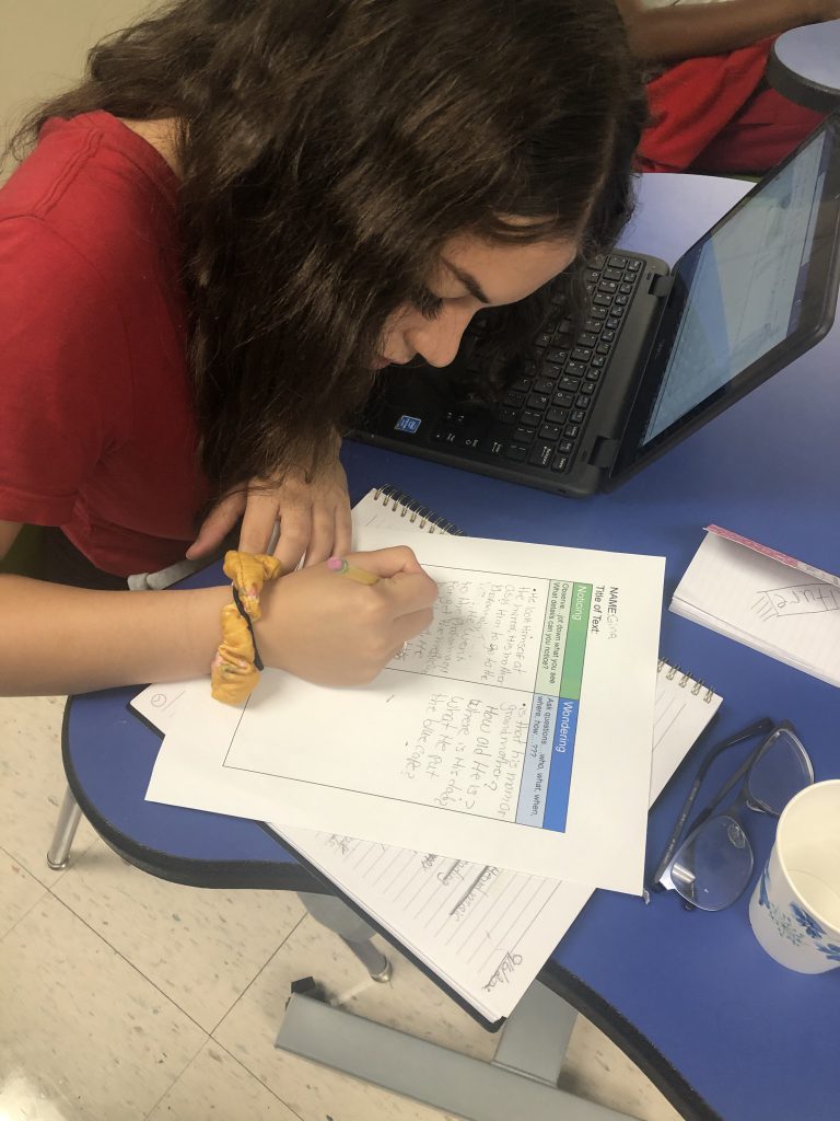 a girl is seated at a desk working on a homework assignment