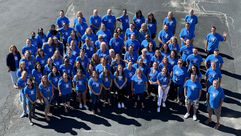 a large group of teachers are posing. They are all wearing blue shirts.