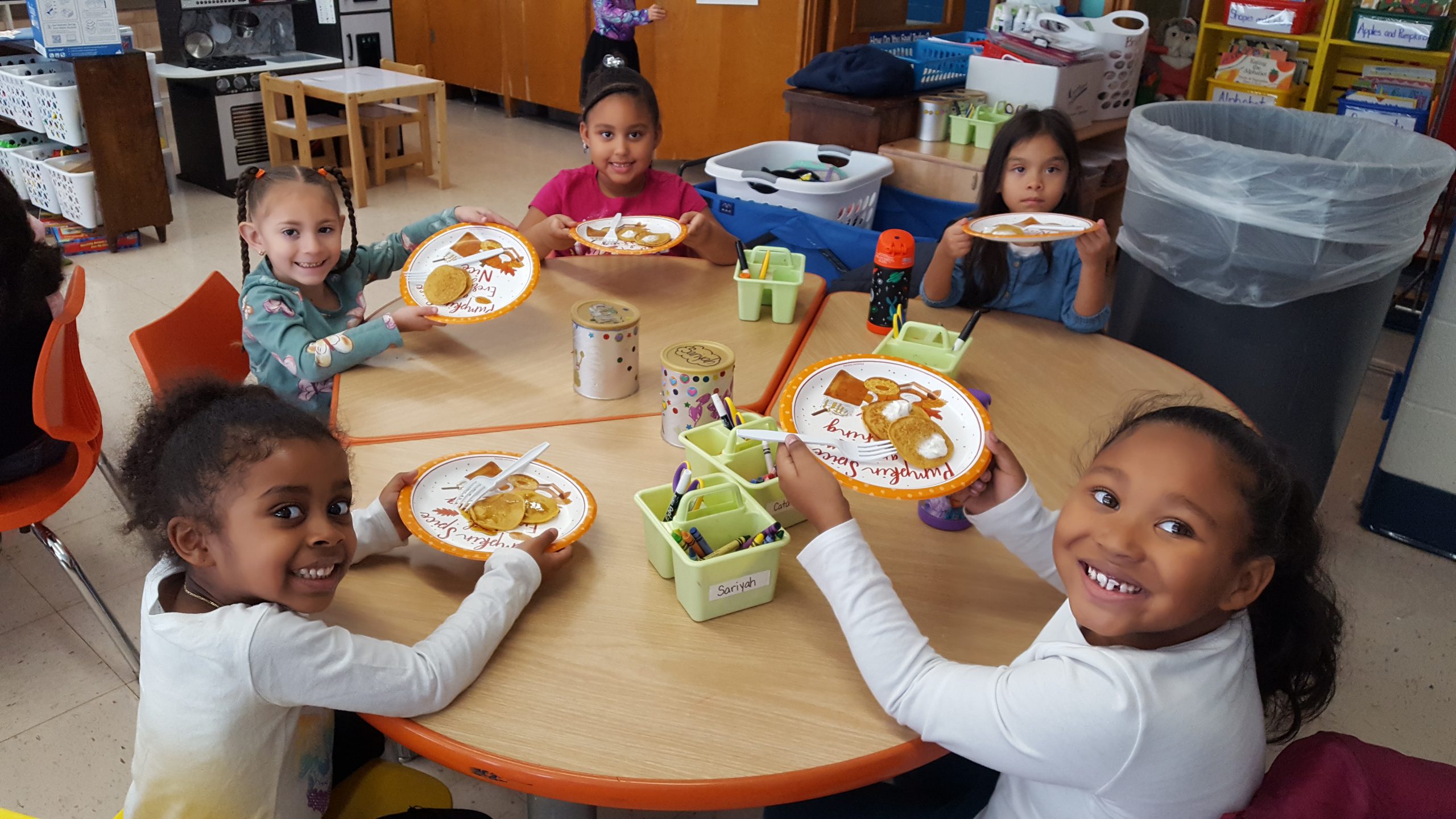 a group of young students are seated around a table. they are all holding up plates with pancakes on them