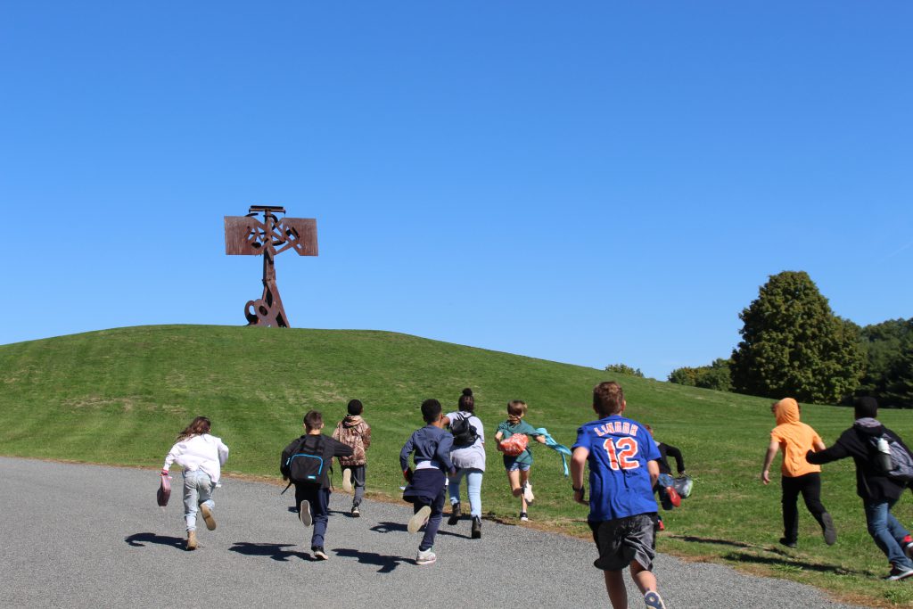 a group of students are running up a hill towards a sculpture