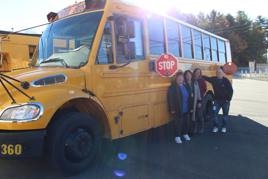 Four members of the administrative team post in front of the bus