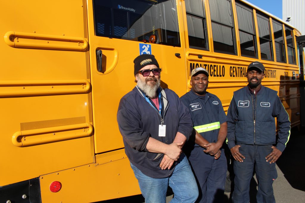 three mechanics pose near a bus