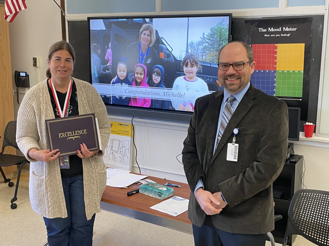 michelle knowlton and Dr. Evans are standing in front of a sign that says congratulations. Michelle is holding up a certificate. 