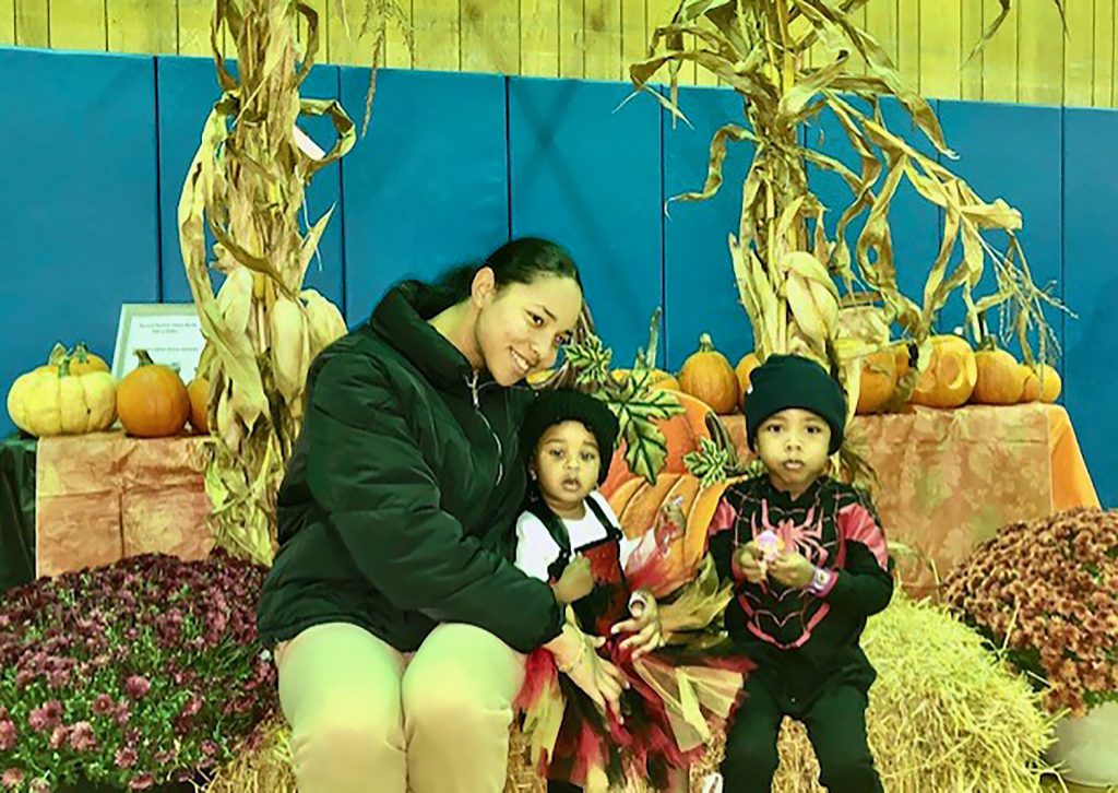 A mother and her two children smiling for a photo on a bale of hay.