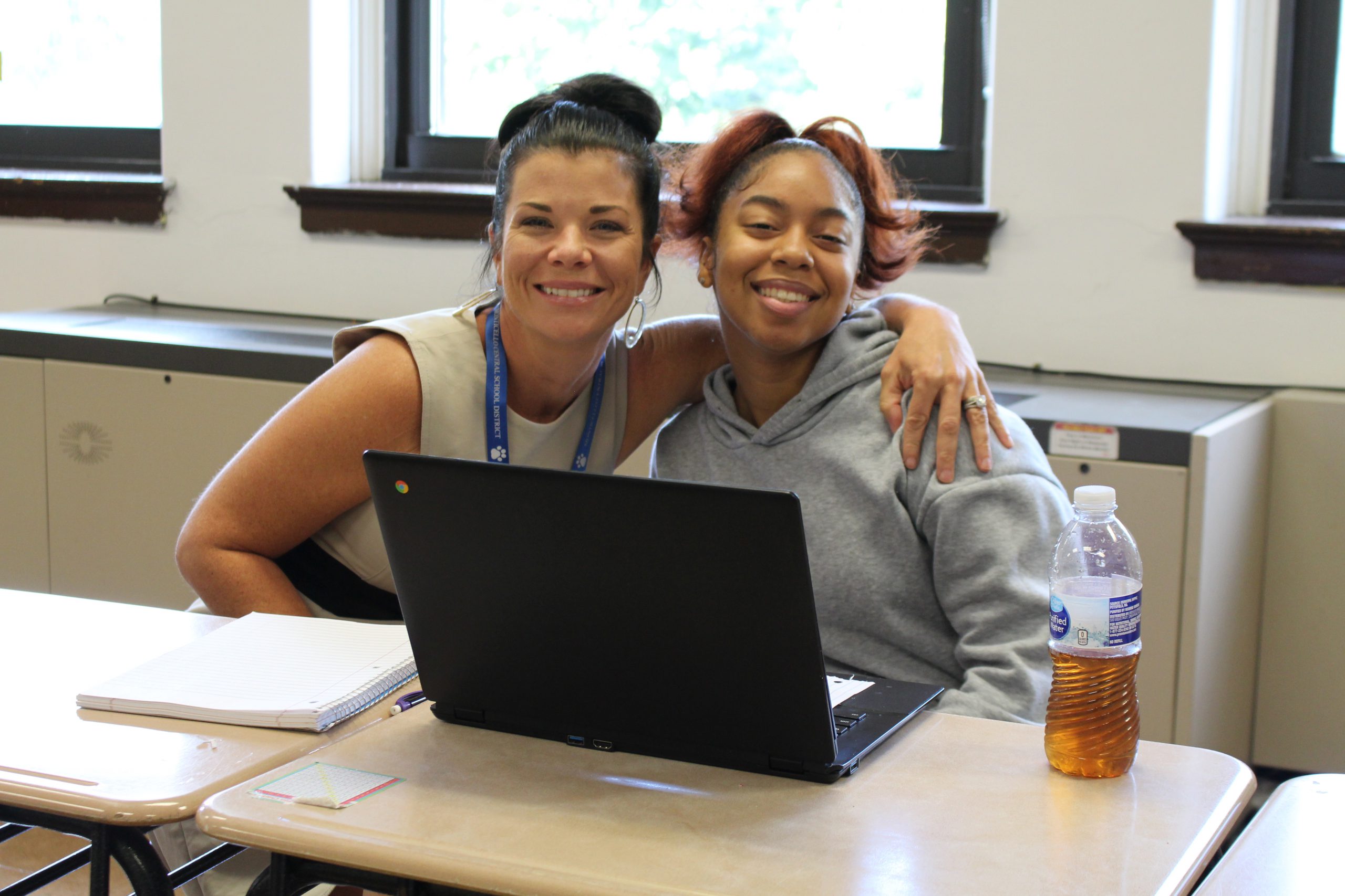 a high school aged student and her principal are seated and smiling. They are embracing.