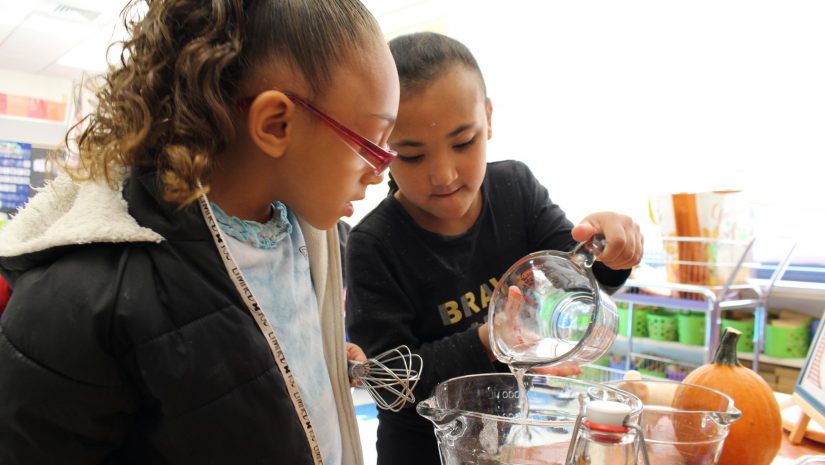 two young girls are working together to pour batter into a mixing cup