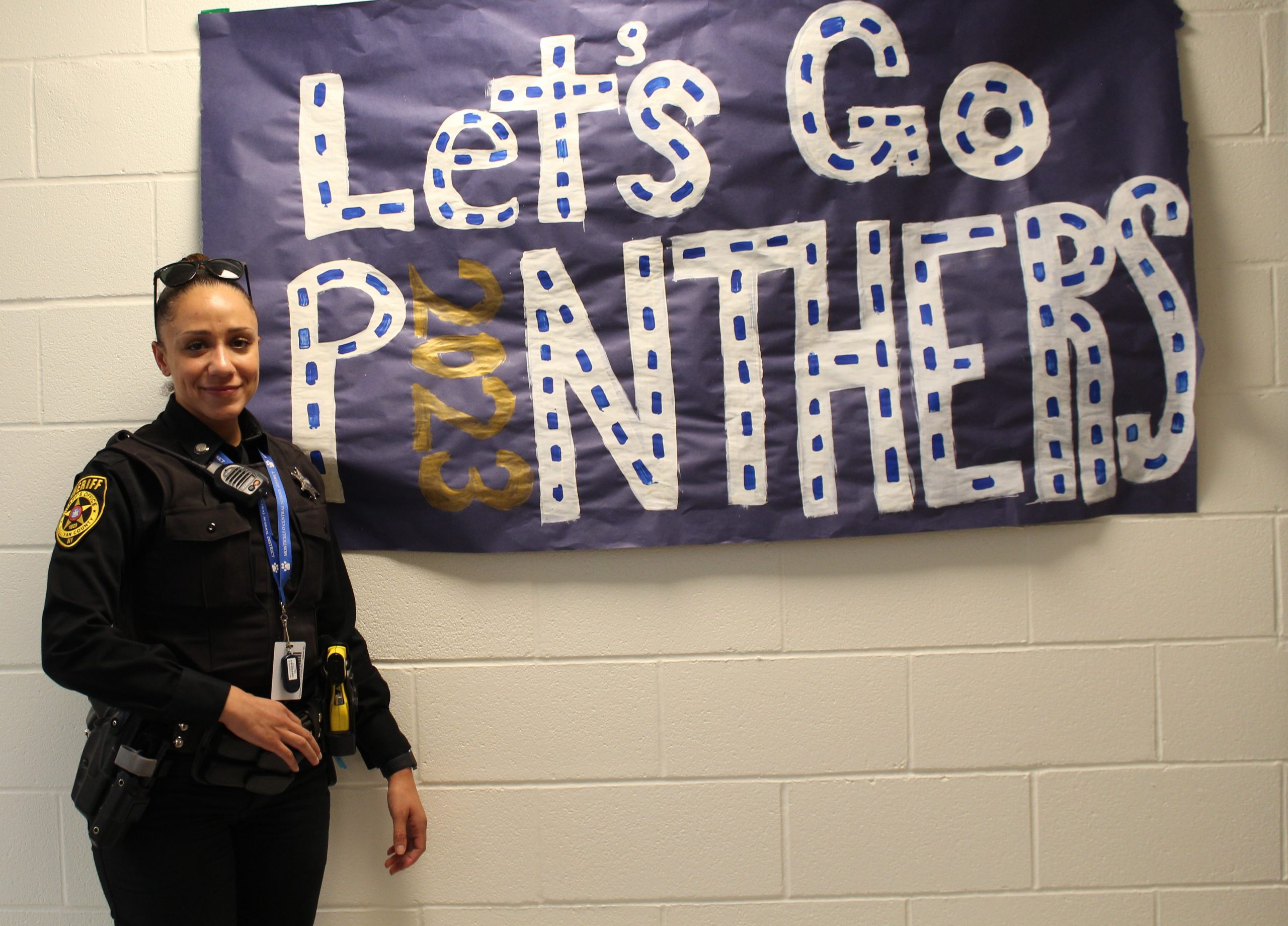 a female police officer is standing in front of a sign that says Lets Go Panthers 