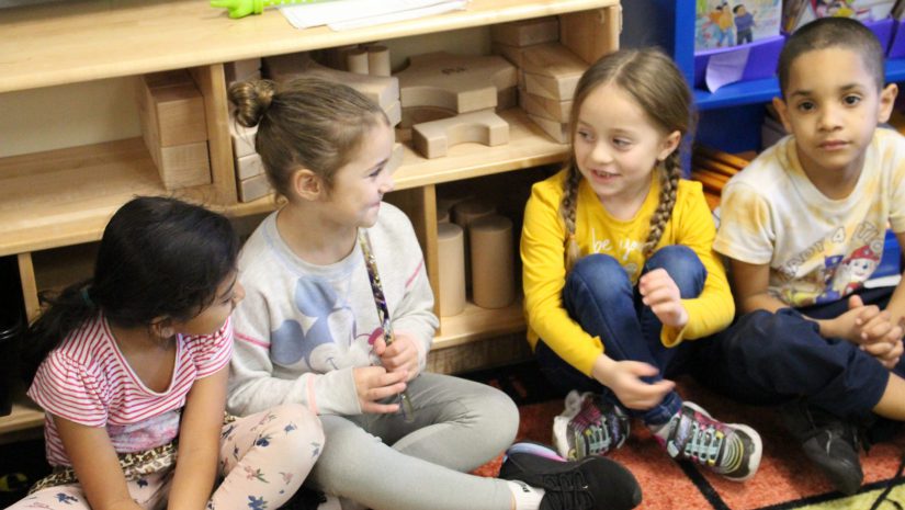 four students are seated in a circle speaking