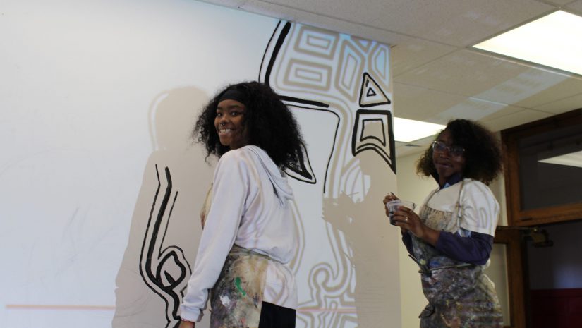 two students are painting a mural on the wall
